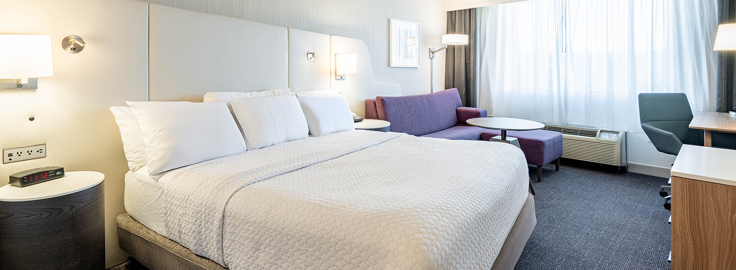 Large king bed with white linens and pillows and a maroon couch with coffee table