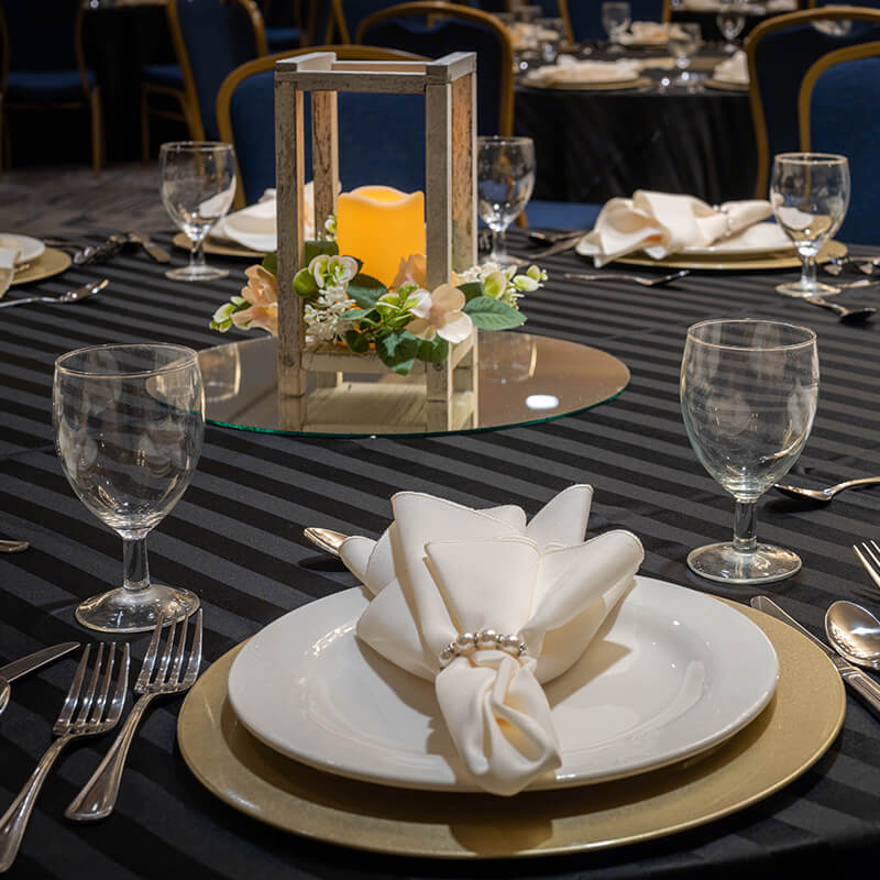Round banquet table with striped gray table cloth, white place settings and a rustic centerpiece with candle