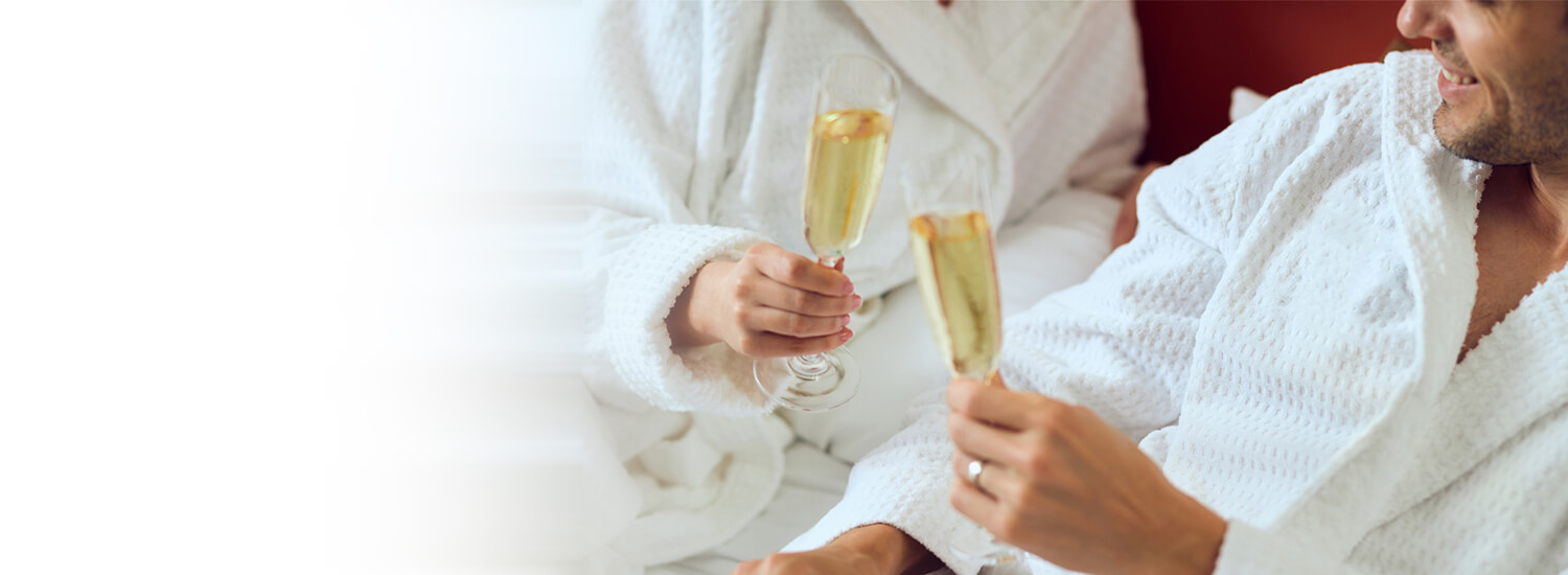 Man and woman in bath robes cheersing champagne glasses