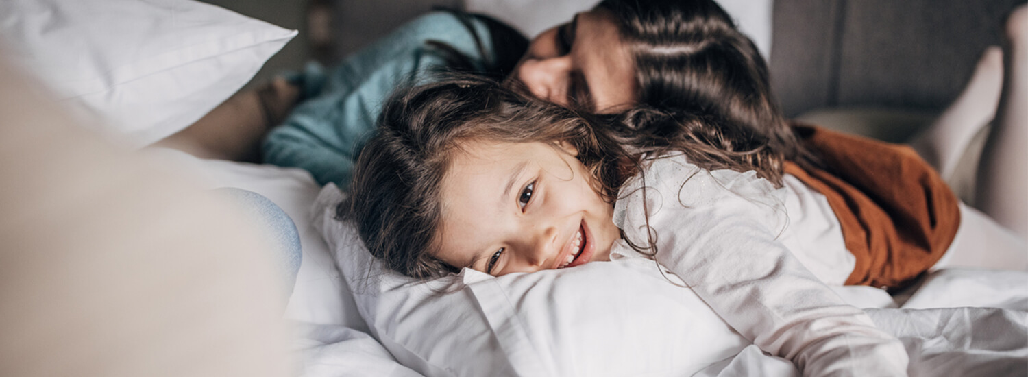 Smiling young girl laying in a hotel bed with her mother