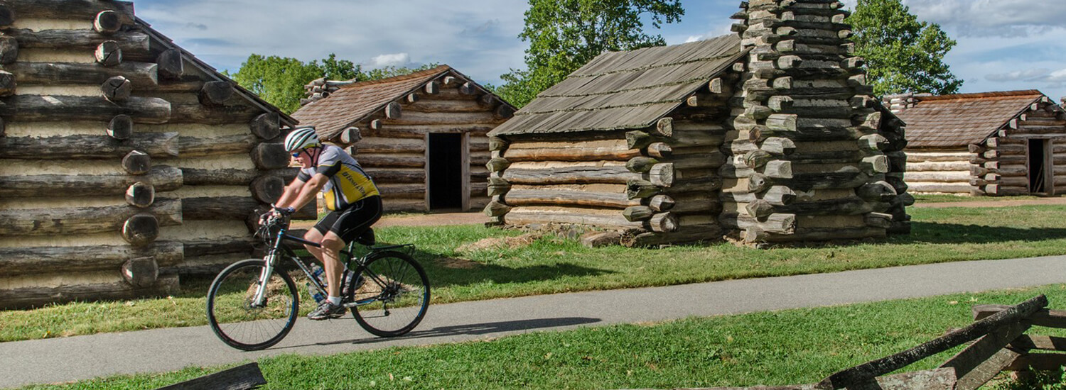 Man cycling on bike path surrounded by log cabins