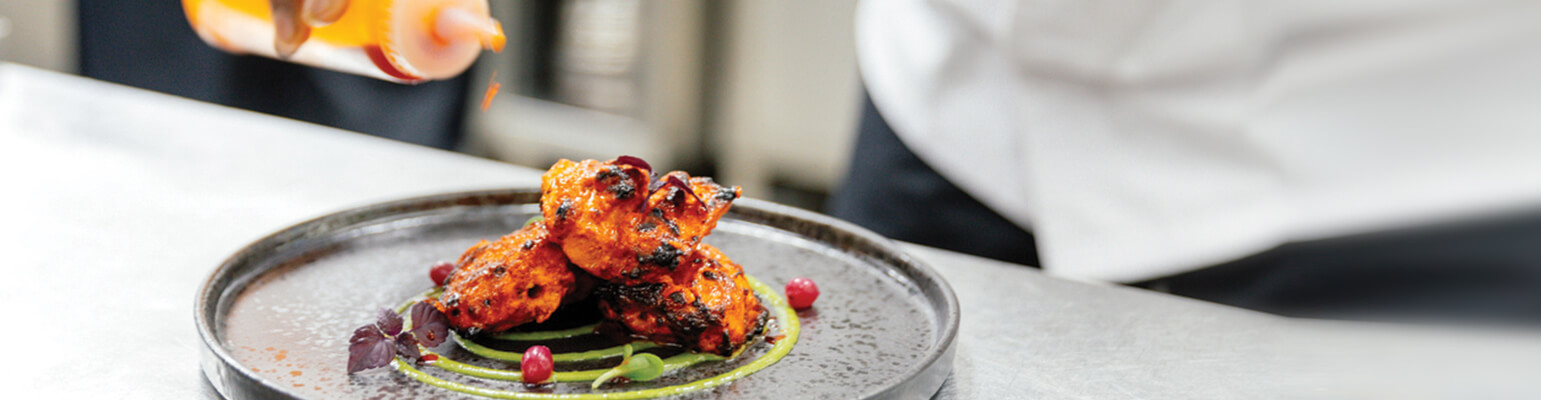 Chicken on metal plate with chef drizzling sauce on it