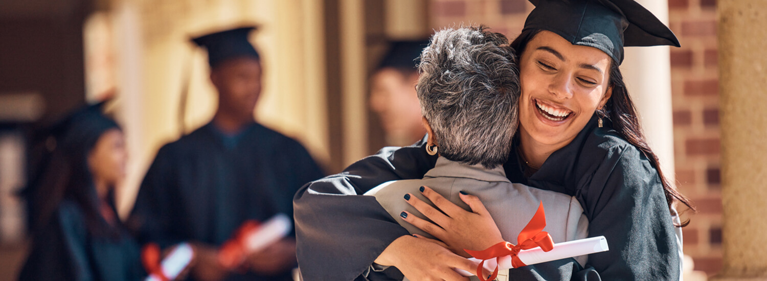 Young woman in graduation cap and gown hugging older woman
