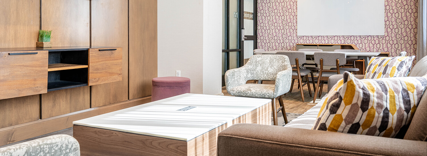 Small meeting room with fancy, comfy chairs, a couch with colorful throw pillows and a small 4 person table