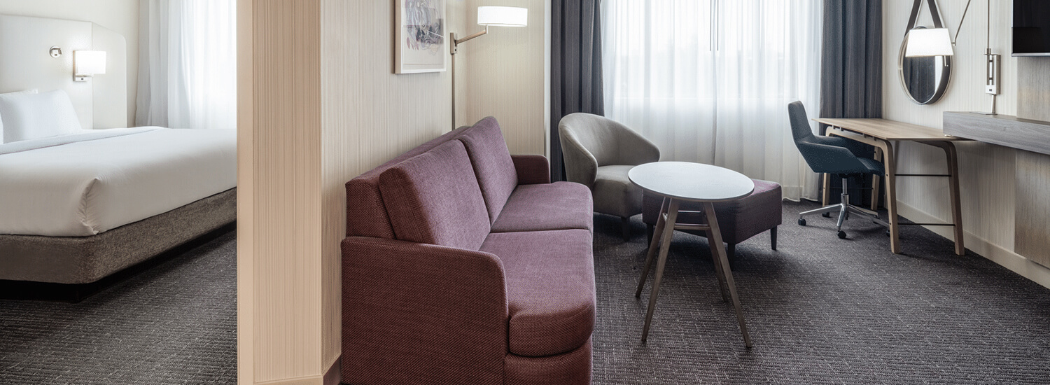Living area of a suite with a maroon couch, coffee table, single person chair, and a desk with office chair