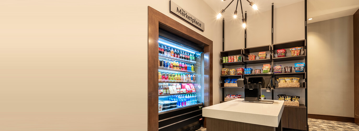 Wall of marketplace with shelves full of snacks next to the a large refridgerator with colorful bottled drinks