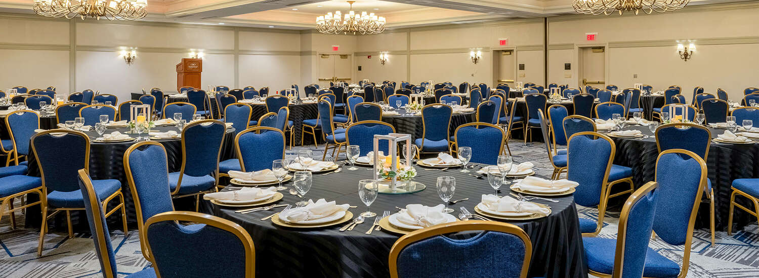 Ballroom filled with tables dorned in gray table clothes and surrounded by glue and gold chairs