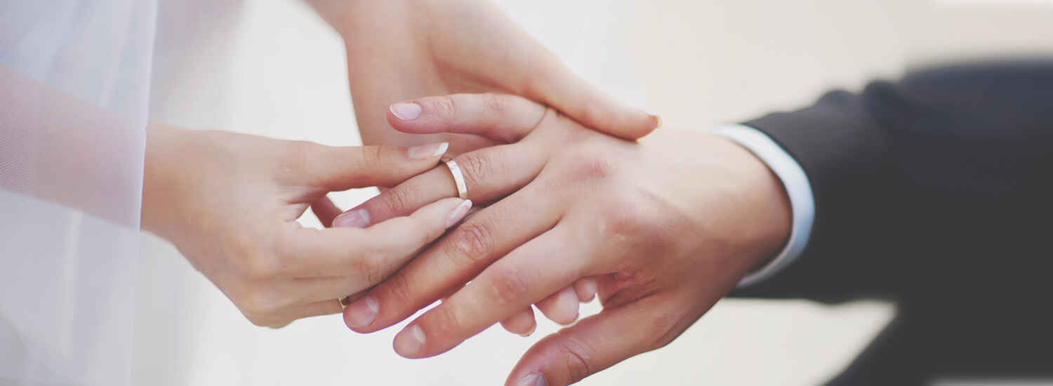 Close up of bride's hand placing a ring on the groom's hand